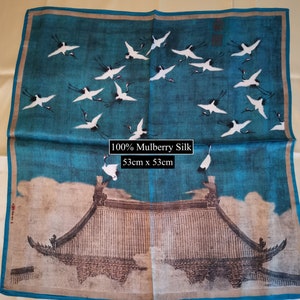 K&ouml;nnte beinhalten: Ein blauer Seidenschal mit einem wei&szlig;en und schwarzen Druck von Kranichen, die &uuml;ber einem traditionellen chinesischen Geb&auml;ude fliegen. Der Schal ist aus 100% Maulbeersilk und misst 53 cm x 53 cm.