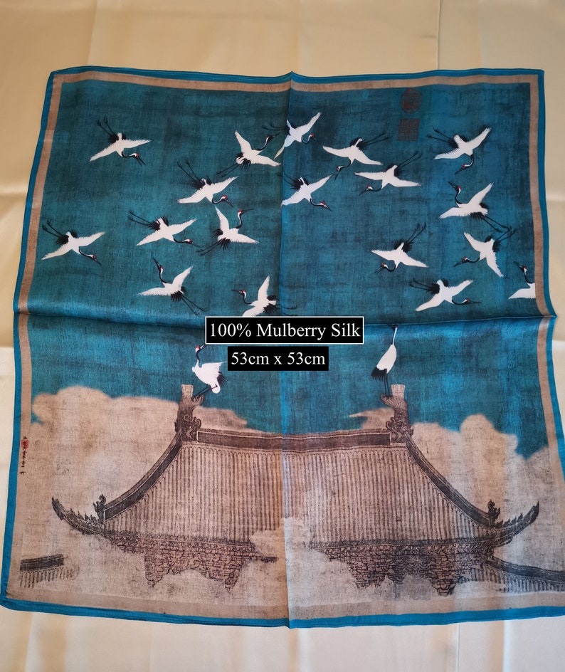 K&ouml;nnte beinhalten: Ein blauer Seidenschal mit einem wei&szlig;en und schwarzen Druck von Kranichen, die &uuml;ber einem traditionellen chinesischen Geb&auml;ude fliegen. Der Schal ist aus 100% Maulbeersilk und misst 53 cm x 53 cm.