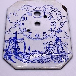 May include: Vintage clock face with a white background and blue illustrations. The design features windmills, clouds, and a seascape. The clock face has numbers from 1 to 12 and the text "THE LUX CLOCK MFG. CO. WATERBURY, CONN. U.S.A."