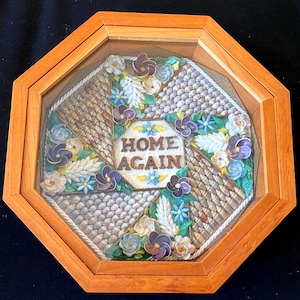 May include: An octagonal wooden framed art piece with a glass cover. The artwork features a central design with the words "HOME AGAIN" surrounded by floral and woven patterns in shades of brown, white, blue, and purple.