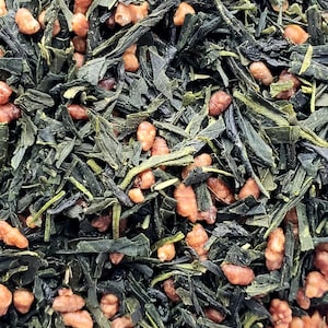 以下が含まれることがあります： 玄米茶のクローズアップ。日本の緑茶と玄米の組み合わせ。濃い緑色の茶葉と、薄茶色のポン菓子のような玄米が混ざり合っています。茶葉は少し光沢があり、玄米は不規則な形をしています。