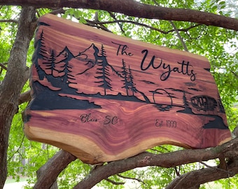 May include: A wooden sign with a carved mountain scene, trees, and a camper. The sign reads "The Wyatts Est. 1999" and "Blair, SC".