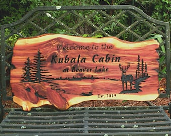 May include: Welcome to the Kubala Cabin at Beaver Lake, a wooden sign with a carved deer and trees, established in 2019.