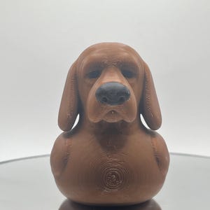 May include: A brown rubber duck shaped like a basset hound with a black nose.