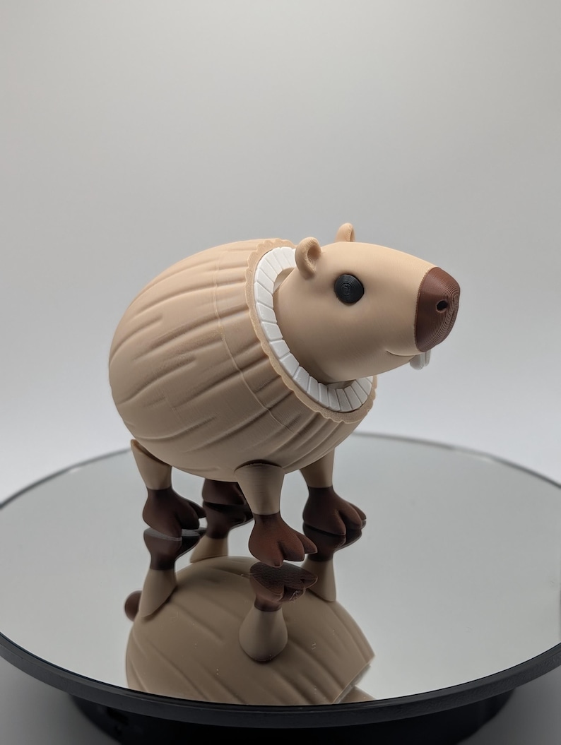 Puede incluir: Una figura de carpincho marr&oacute;n con un collar blanco. La figura tiene patas marrones y una nariz marr&oacute;n. El carpincho est&aacute; de pie sobre una superficie reflectante. La figura es una representaci&oacute;n estilizada del animal.