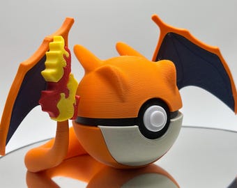 May include: Orange and black 3D printed Pokemon figure of Charizard in a Pokeball. The figure has a yellow and red flame design on its back.