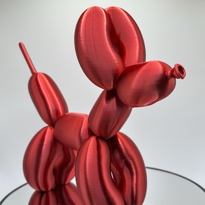 May include: A red balloon animal sculpture in the shape of a dog. The sculpture is made of multiple balloon shapes and has a shiny, glossy finish.
