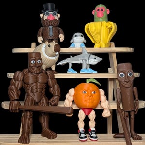 Puede incluir: Una colecci&oacute;n de figuras caprichosas exhibidas en una estanter&iacute;a de madera. Las figuras incluyen un tibur&oacute;n, un mono en un pl&aacute;tano, un carpincho, un hombre con traje, un delf&iacute;n, una figura musculosa con un bate, una naranja con brazos y piernas y una figura de madera.