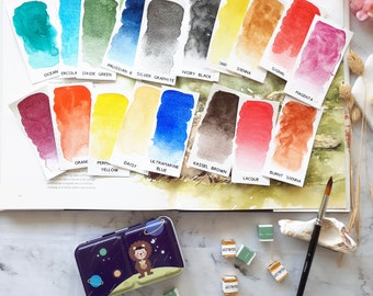 May include: A watercolor paint set with a variety of colors, including ocean, ercola oxide green, Prussian & silver graphite, ivory black, burnt sienna, kassel brown, laque, ultramarine blue, signal, sienna, magenta, daisy, perma yellow, orang, and more. The set comes in a metal tin with a cartoon lion design.