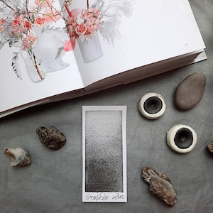 May include: A close-up of a small, rectangular card with a gray gradient background. The card is labeled "Graphite Silver" in black handwriting.