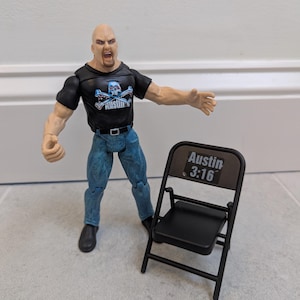 May include: A Stone Cold Steve Austin action figure in a black t-shirt with a skull and crossbones design, blue jeans, and black boots. A black folding chair with "Austin 3:16" printed on the back is next to the figure.
