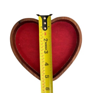 Puede incluir: Una caja de madera en forma de coraz&oacute;n con un forro interior de terciopelo rojo. Una cinta m&eacute;trica amarilla DeWalt est&aacute; colocada verticalmente sobre el centro de la caja, mostrando una medida de aproximadamente 14,6 cm desde el borde superior al inferior.