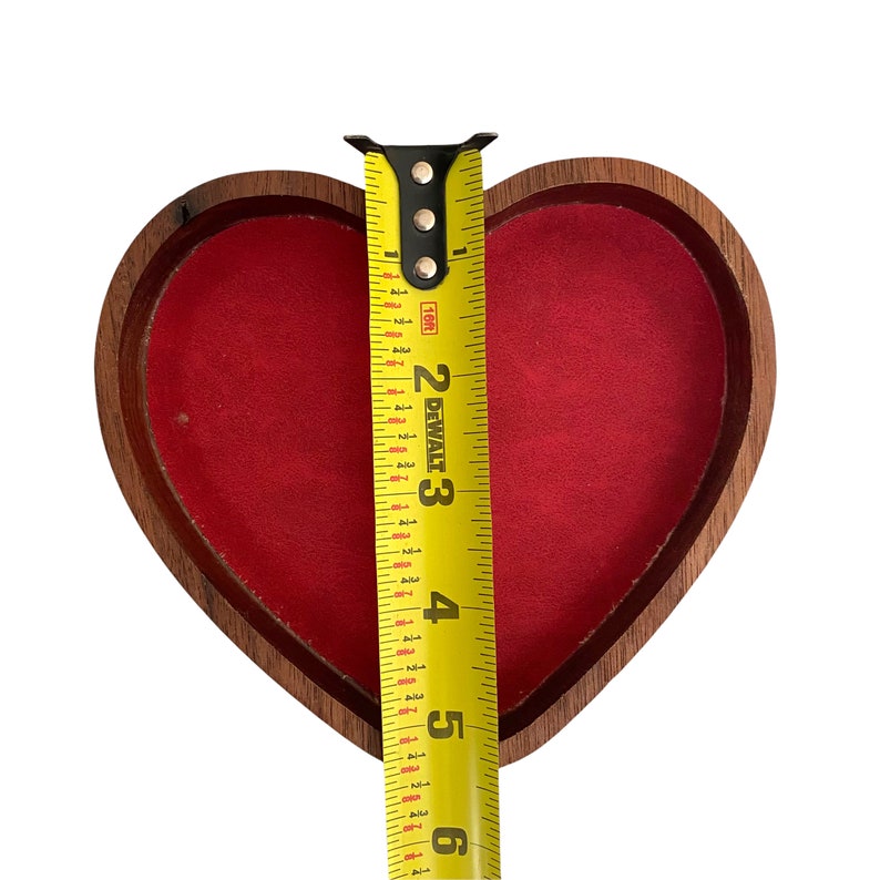 Puede incluir: Una caja de madera en forma de coraz&oacute;n con un forro interior de terciopelo rojo. Una cinta m&eacute;trica amarilla DeWalt est&aacute; colocada verticalmente sobre el centro de la caja, mostrando una medida de aproximadamente 14,6 cm desde el borde superior al inferior.