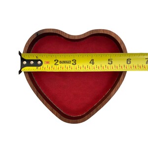 Puede incluir: Un cuenco de madera en forma de coraz&oacute;n con un forro interior rojo. Una cinta m&eacute;trica amarilla DeWalt est&aacute; colocada en el centro, mostrando un ancho de aproximadamente 16,5 cm desde el borde izquierdo hasta el derecho del marco de madera.