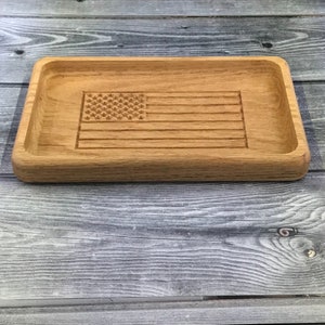 May include: A wooden tray with an American flag design carved into the surface. The tray is made of light brown wood and has a rectangular shape.