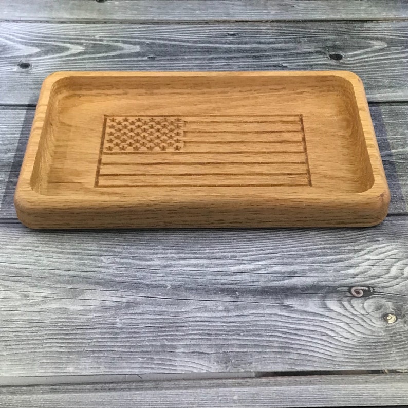 May include: A wooden tray with an American flag design carved into the surface. The tray is made of light brown wood and has a rectangular shape.