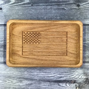 May include: A wooden tray with a carved American flag design. The tray is made of light brown wood and has a rectangular shape.