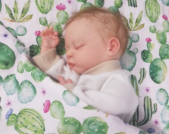 May include: A baby sleeping on a white sheet with a cactus print. The sheet has green and pink watercolor cactus illustrations.