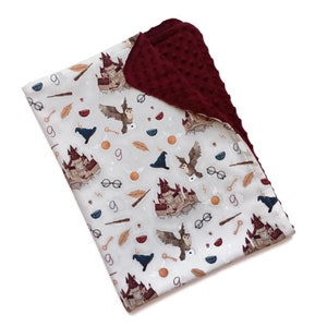 May include: A baby blanket featuring a light gray pattern with illustrations of owls, castles, keys, and other magical elements. The blanket has a burgundy, textured backing. The blanket is designed with a whimsical theme.