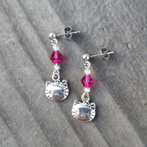 May include: A pair of silver Hello Kitty earrings with pink crystal accents.