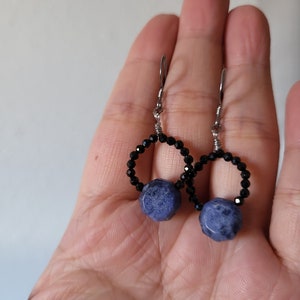 May include: A pair of earrings with a blue gemstone and black beads. The earrings are made with silver wire and have a simple design.