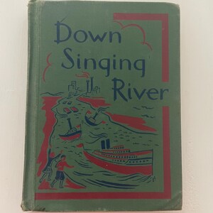 May include: A vintage book titled "Down Singing River" with a green cover and red and blue illustrations. The cover art depicts boats on a river with figures on the shore. The book's title is in a stylized font.