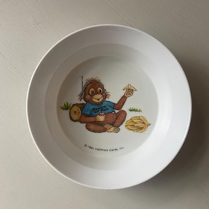 May include: A white ceramic bowl featuring a cartoon orangutan wearing a blue shirt with the text BUNCH OF FUN. The orangutan wears headphones, holds a banana, and sits near a log and a pile of bananas. The text 1981 Hallmark Cards, Inc. is printed.