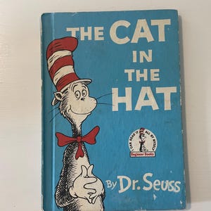 May include: A vintage copy of "The Cat in the Hat" by Dr. Seuss. The book cover is light blue with the title in large white letters. The Cat character is illustrated with a red and white striped hat, a red bow tie, and white gloves.