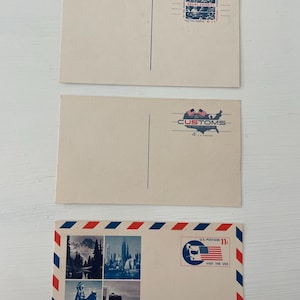 May include: Three vintage postcards. The top two are blank on the front with postage stamps. The bottom postcard has a red, white, and blue border, four images, and a postage stamp that says "Visit the USA".