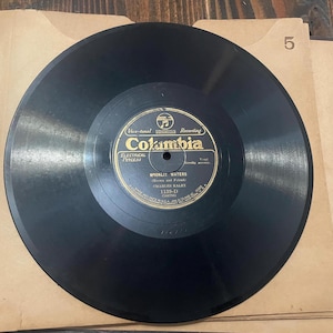 May include: A vintage black vinyl record with a gold and black label from Columbia Records. The label features the text "Moonlit Waters" by Charles Kaley. The record is in a tan paper sleeve, with the number "5" visible.