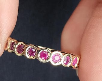 May include: A gold band ring with a row of pink gemstones. The ring is set with round, bezel-set stones.