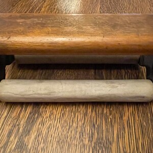 May include: A wooden and metal paper towel holder with a white paper towel roll. The holder has a dark brown wooden top and black metal sides.