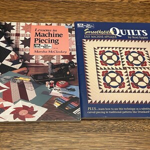 May include: Two quilting books are displayed on a wooden surface. The book on the left is titled "Lessons in Machine Piecing" by Marsha McCloskey. The book on the right is titled "Smoothstite Quilts" by Roxi Eppler. Both books feature colorful quilt designs.