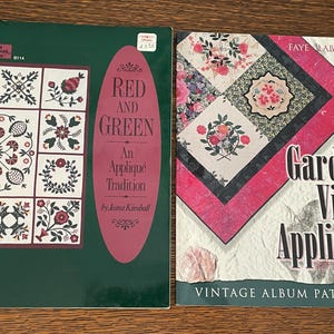 May include: Two books on a wooden surface. The first, green, features floral quilt patterns and the text "Red and Green: An Appliqué Tradition." The second, pink and white, is titled "Garden View Appliqué" with vintage album patterns.
