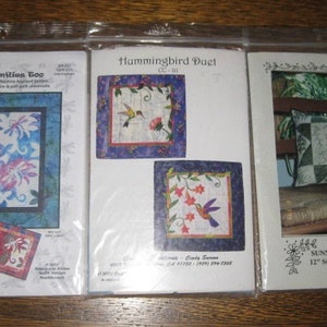 May include: Three different quilting patterns, Dragonflies Eco, Hummingbird Duet, and Sunny Garden 17" Stitchery Pillow. Each pattern is printed on a white background with a colorful image and text.