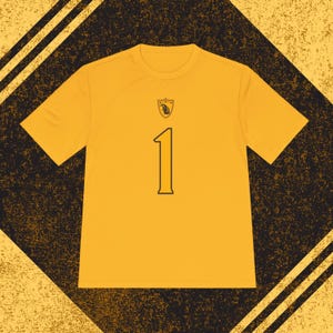 Pode incluir: Camiseta amarela mostarda de manga curta com o número 1 preto na frente. Um pequeno emblema está posicionado acima do número. A camisa é feita de um tecido leve e respirável, adequado para esportes ou uso casual.