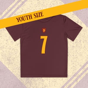 May include: A maroon youth-sized t-shirt with a gold number 7 on the front. The shirt has a small emblem above the number and a yellow banner that reads "YOUTH SIZE".