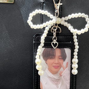 May include: A black cardholder with a photo, attached to a black handbag with a pearl bow and a silver clasp. The cardholder has a photo of a person. The pearl bow is made of white pearls.