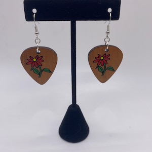 May include: A pair of wooden earrings shaped like guitar picks with a red flower painted on each. The earrings have silver hooks.