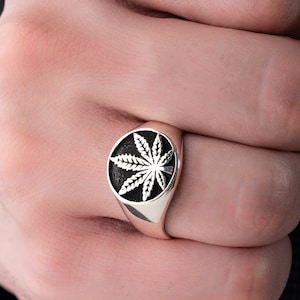 May include: A silver ring featuring a black and white marijuana leaf design.