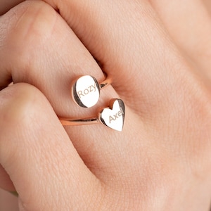 Könnte beinhalten: Ein goldfarbener Ring mit zwei gravierten herzförmigen Anhängern. Die Anhänger sind mit den Namen "Rozy" und "Axel" graviert.