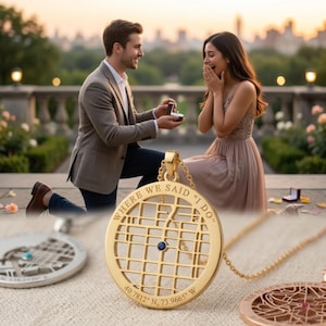 May include: A gold-colored pendant necklace with a map design and the text "WHERE WE SAID 'I DO'". The pendant features a grid pattern with a blue gemstone and the coordinates 40.7812° N, 73.9665° W. A couple is in the background.