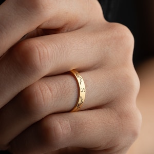 Könnte beinhalten: Ein goldener Bandring mit einem zarten Blattdesign und dem Buchstaben "S" auf der Band graviert.