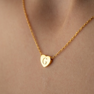 May include: A gold chain necklace with a heart-shaped pendant featuring the letter "G" engraved on it.