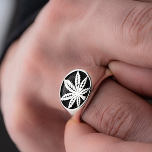 May include: A silver ring with a black and white marijuana leaf design.