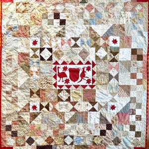 May include: A patchwork quilt with a variety of fabric patterns in beige, brown, and red hues. The quilt features a central red square with a white border and a red design. The border is red with a scalloped edge.