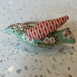 May include: A green and pink fabric bird pincushion with a floral pattern. The pincushion is filled with pins and is ideal for sewing.