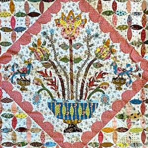 Può includere: Una trapunta vintage con un motivo floreale al centro. La trapunta è realizzata in tessuto patchwork di vari colori e motivi. Il motivo floreale è circondato da una cornice a forma di diamante con un bordo a festoni.