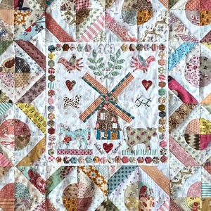 Könnte beinhalten: Eine weiße Steppdecke mit Patchwork-Muster, das verschiedene florale und geometrische Muster zeigt. Das mittlere Quadrat zeigt eine Windmühle, ein Pferd, eine Kuh und den Text "DCD 2023" und "Hickville Detroit".