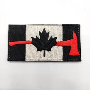 May include: Embroidered patch with a black maple leaf and a red axe on a white and black background. The rectangular patch has a stitched border. The design is inspired by the Canadian flag.